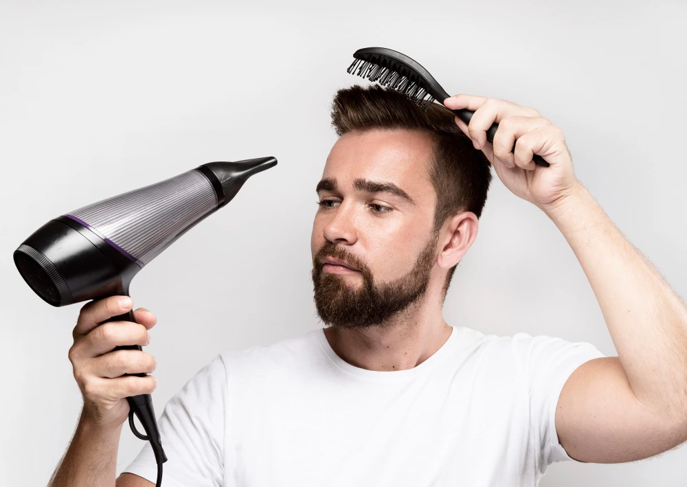 Man at home drying hair with a blow dryer using heat protectant, everyday hair care to prevent breakage