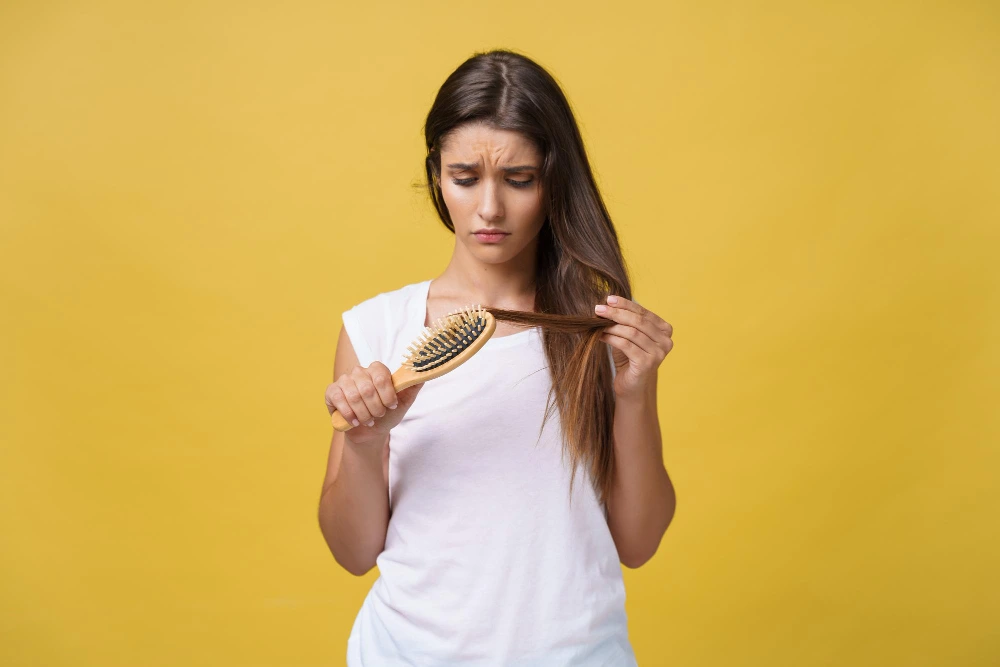 postpartum hair loss: woman brushing hair and seeing strands on the brush